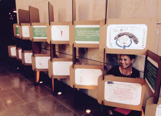 Woman crouches behind display of children's drawings