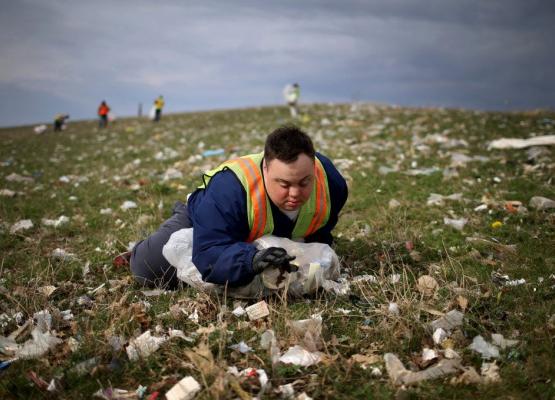 Young man with Down syndrome lying in field of garbage picking up trash