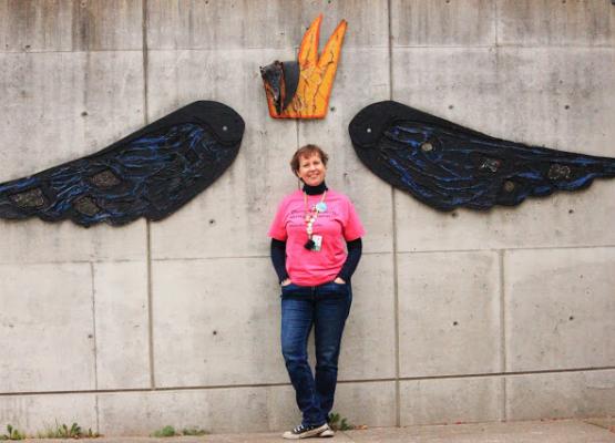 A women standing by a wall with wings and crown behind her