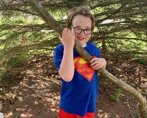 Wesley in a Superman shirt holding up a large branch.