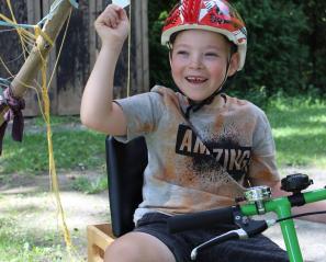 Young boy riding an adaptive bike holding up playing cards. 