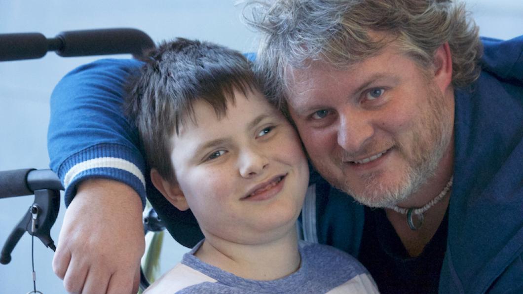 Dad with arm around school-aged son in wheelchair