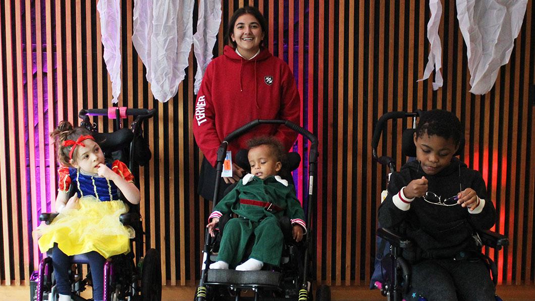 A teenager standing in a backdrop background with three younger children, who are all sitting in wheelchairs