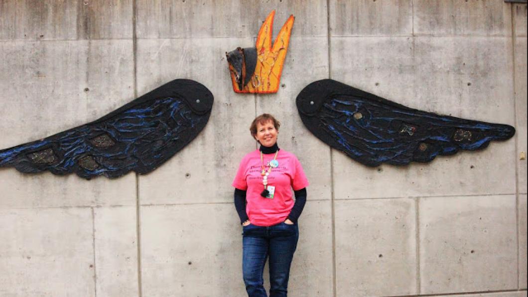 A women standing by a wall with wings and crown behind her