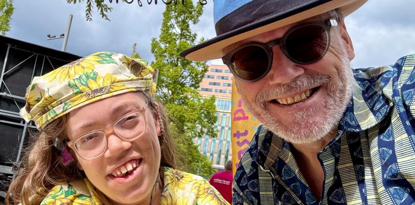 Girl with yellow sunflower hat and shirt smiles with man with blue brimmed hat and sun glasses
