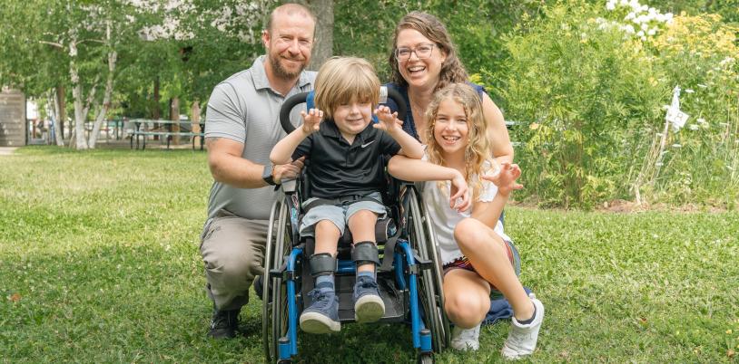 Boy outside in wheelchair beside girl with man and woman behind