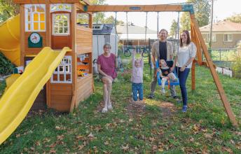 Young child wearing oxygen prongs in a swing beside a girl hanging from a bar with three adults in the background