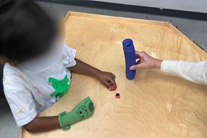 Pinch to pickup small objects from table to drop inside a paper towel roll.