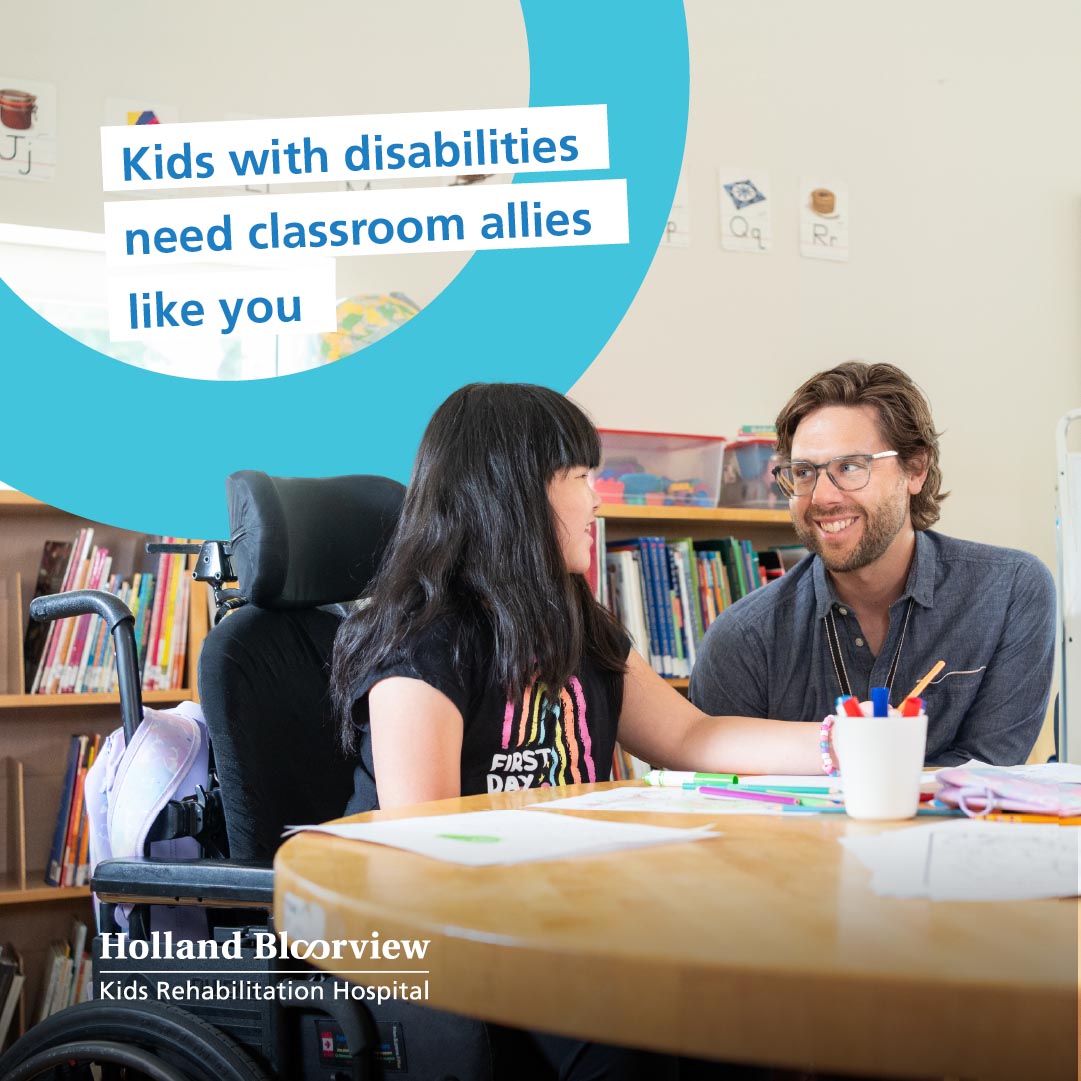 A child using wheelchair is sitting beside an adult, in a library/classroom setting