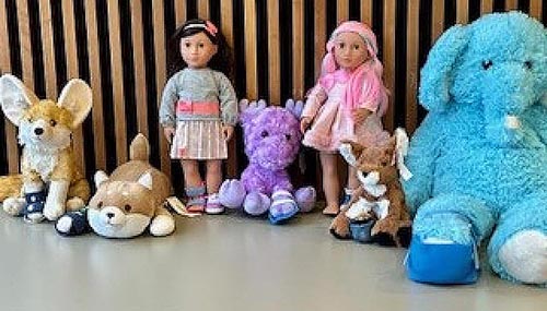 5 stuffed animals and two dolls lined up against a wall wearing splints.