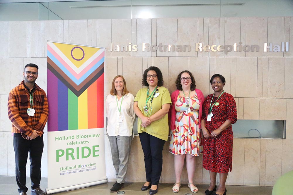 A group of people standing with a PRIDE banner in an indoor setting