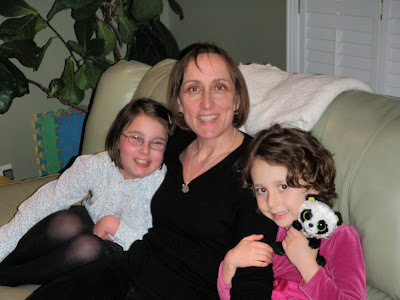 Woman with dark hair sits with a girl snuggled up on each side of her on a couch