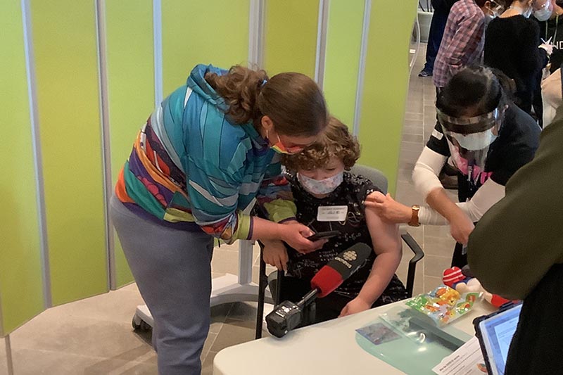 A child with mask is checking something on a mobile phone with an adult