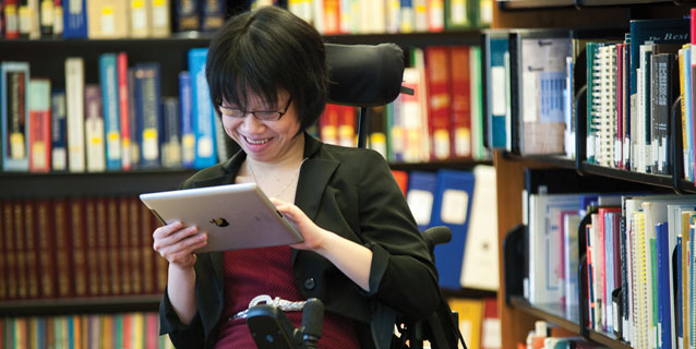 Girl in a wheelchair in the library using a computer tablet.