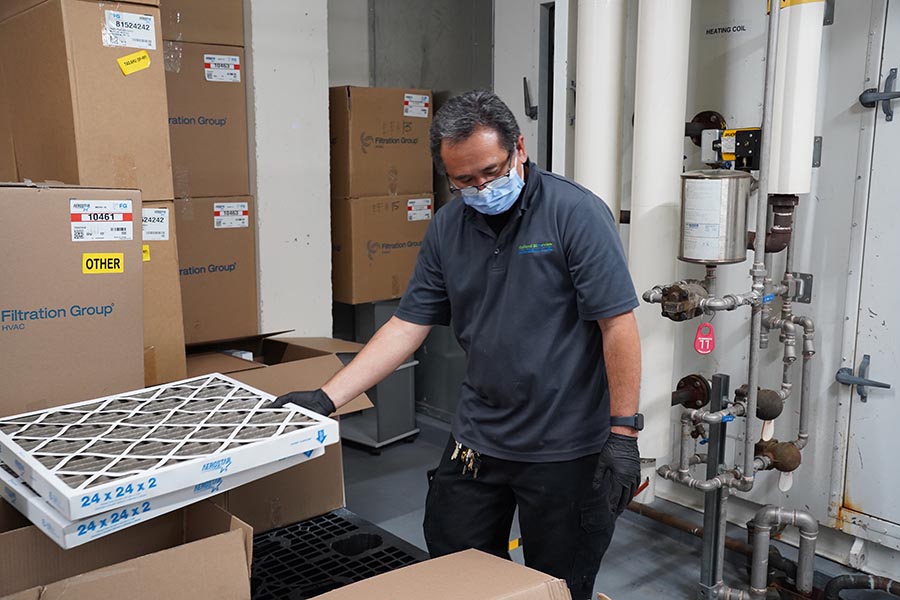 A man with mask on changing filter of a furnace