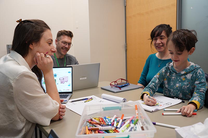 Some adults are getting a child to draw some picture on papers