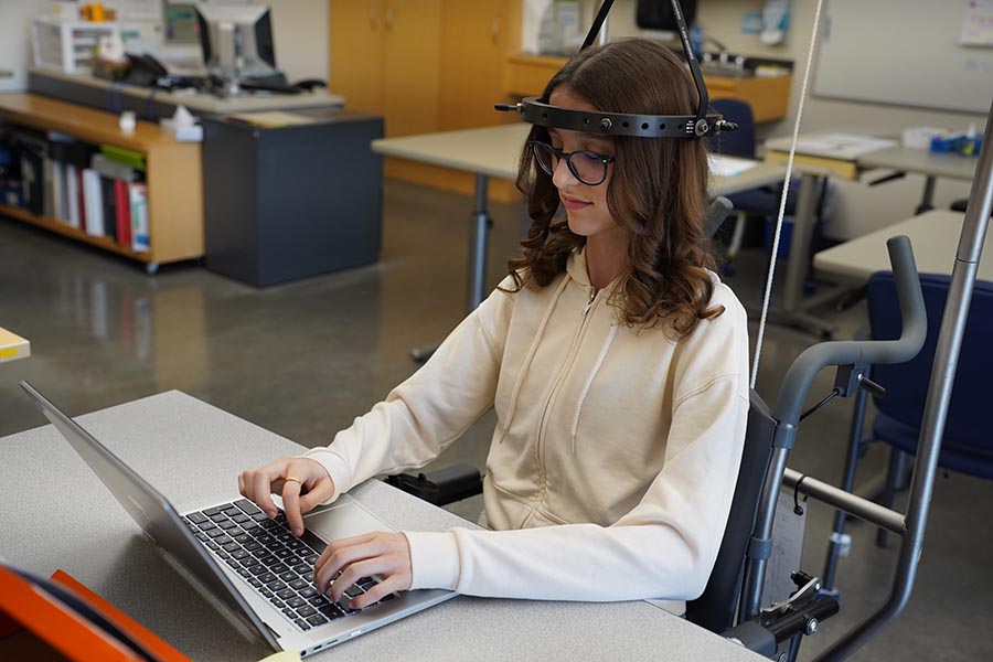 A teen on a wheelchair is typing on a computer