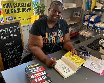 Woman sits at table signing books