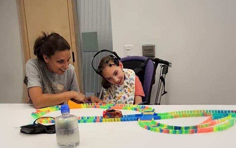 A child in a wheelchair wearing a BCI headset playing with a car