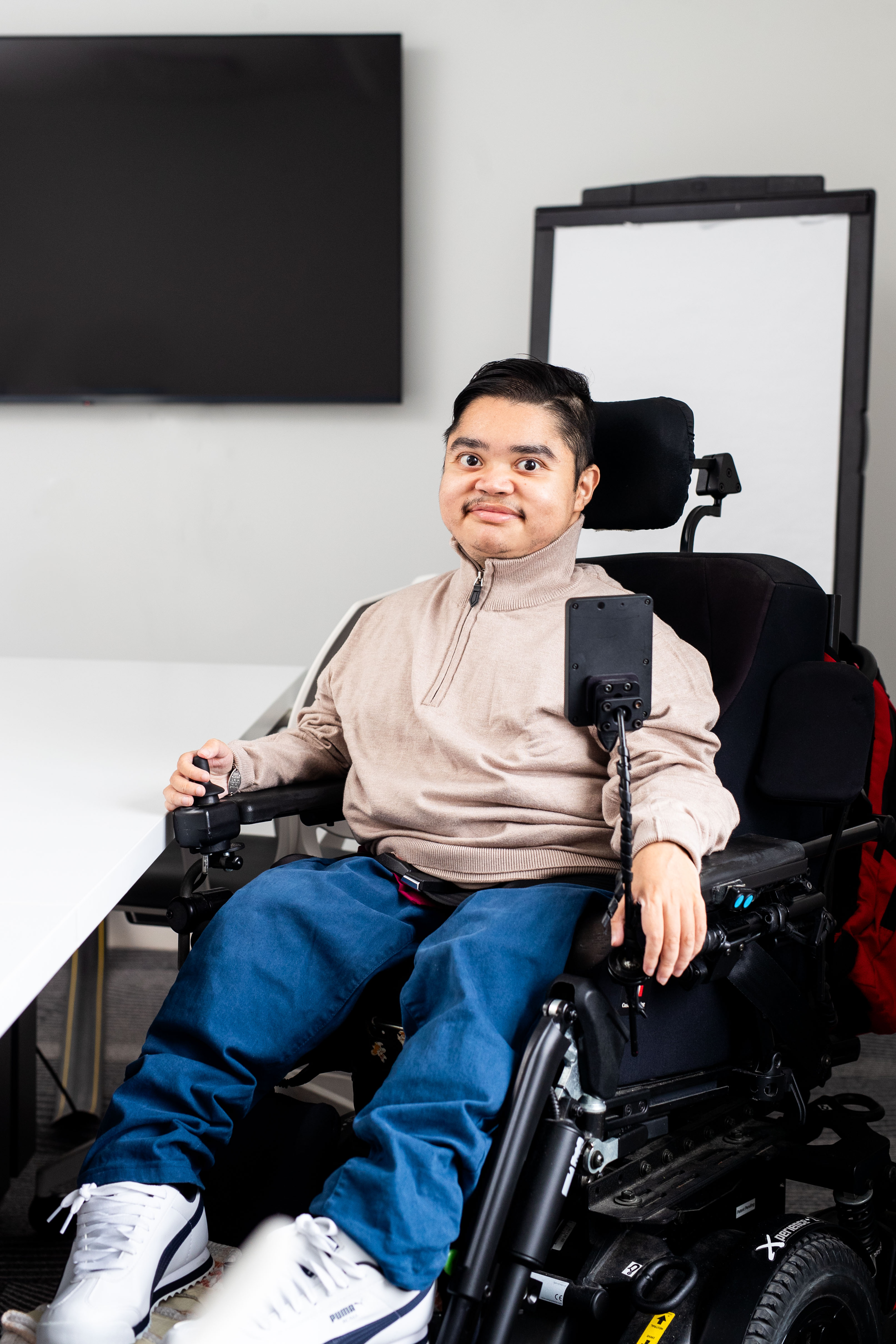 Ivan, who uses a powerchair, poses for a photo beside a desk