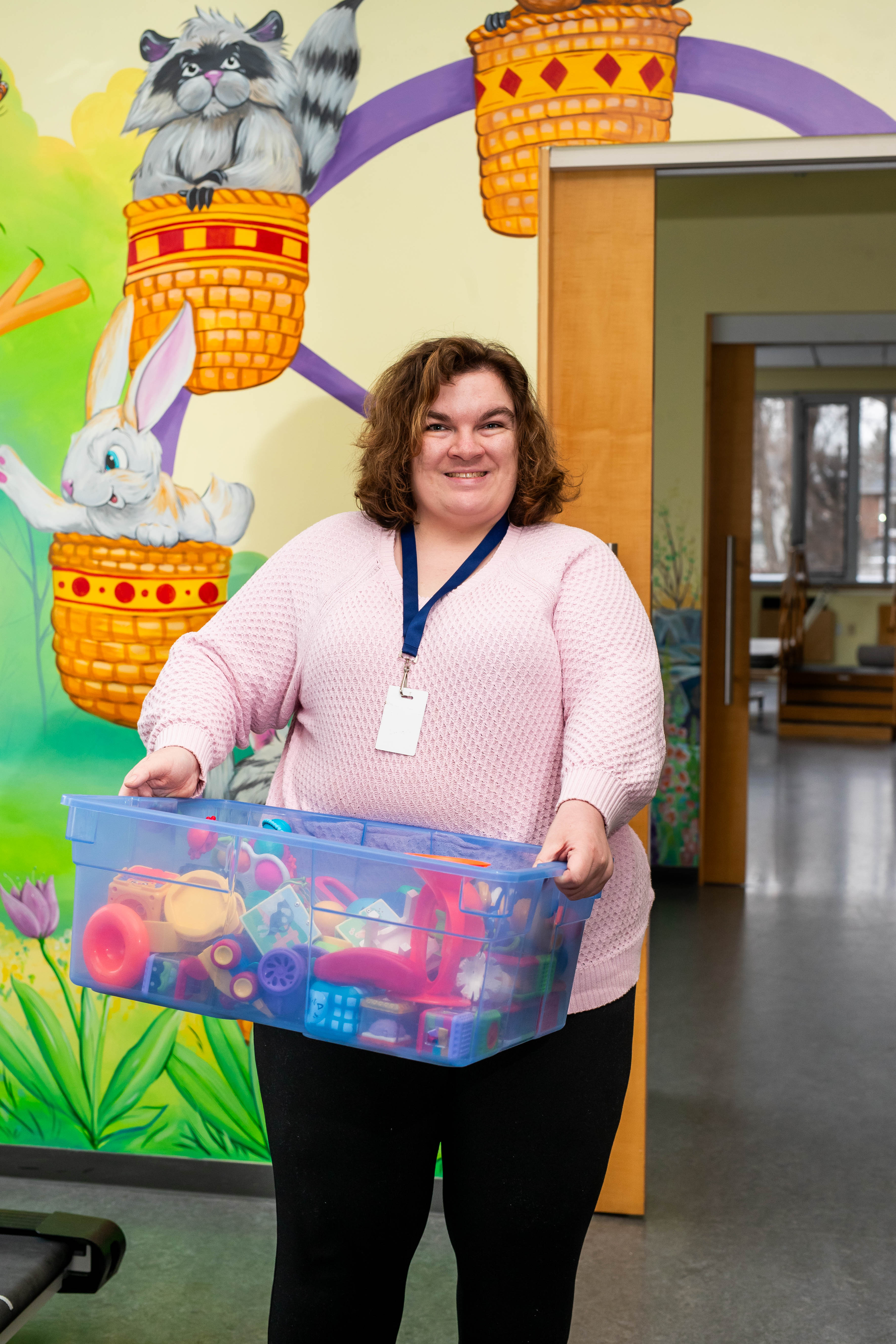 Madeline standing in a doorway, holding a large bin of toys in both hands