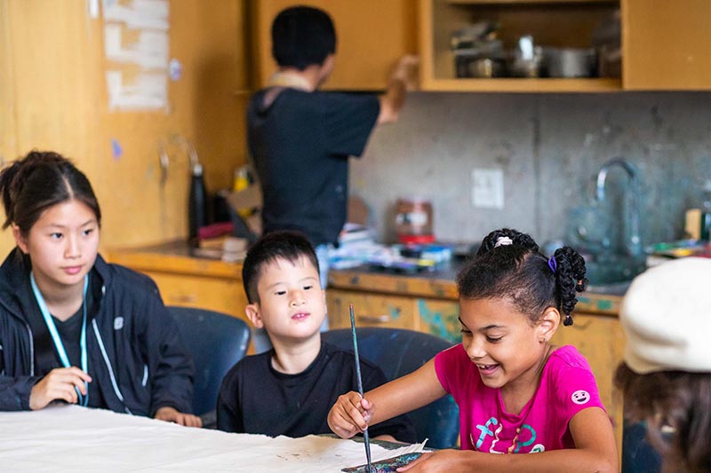 A teenager is teaching two children to draw