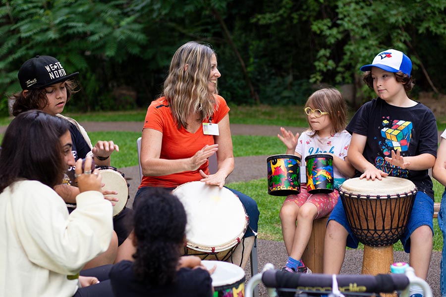 An adult playing drum with some children in an outdoor setting