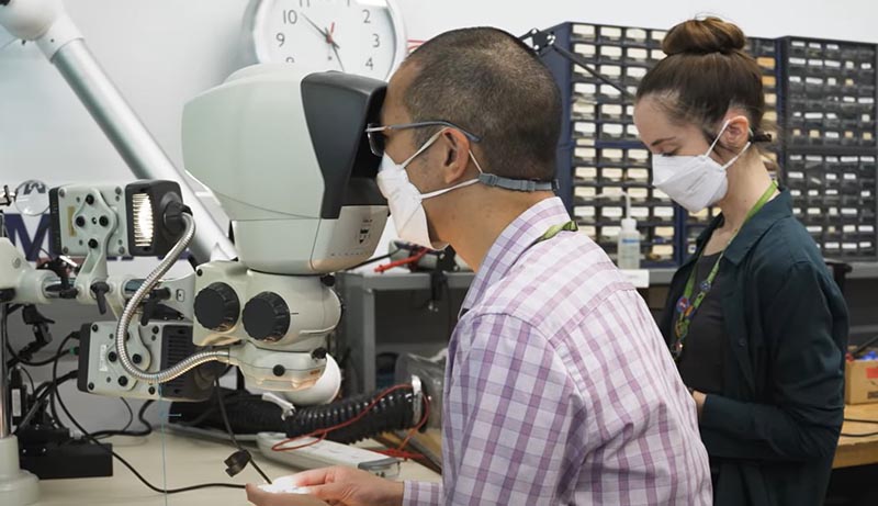 Two adults with mask on working in a lab with a machine