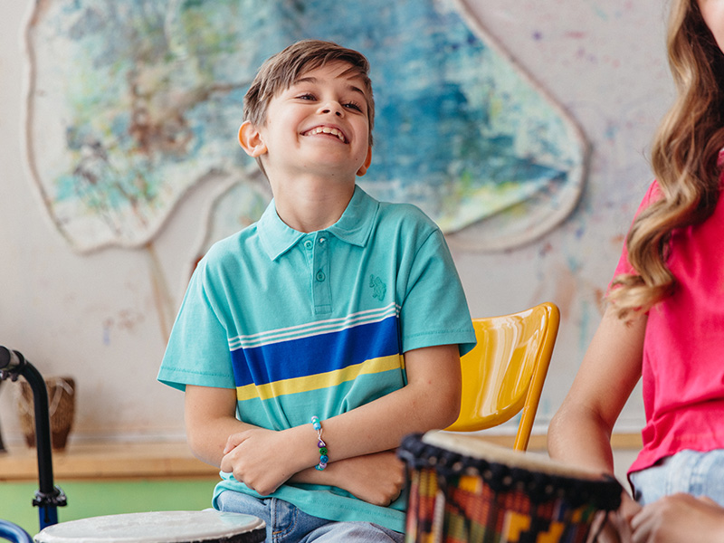 A young boy smiles and plays a drum
