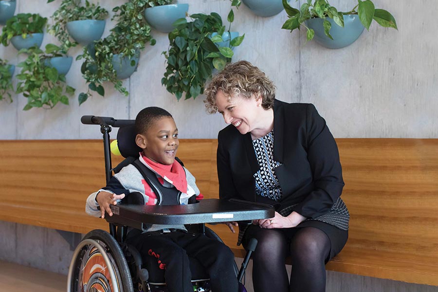 Julia Hanigsberg smiles alongside a photo of a young client early in her 10-year-tenure ad Holland Bloorview’s president and CEO.