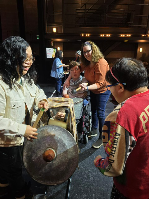 Man in wheelchair plays drum with others looking at instruments