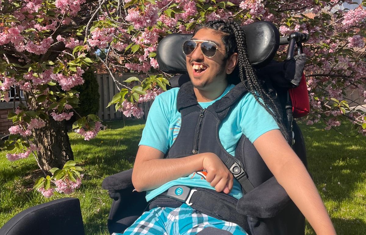 A teen outside sitting in a wheelchair, in front of a tree
