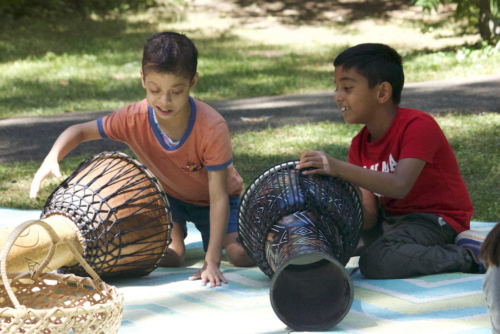 Two boys with dark hair play drums on blanket