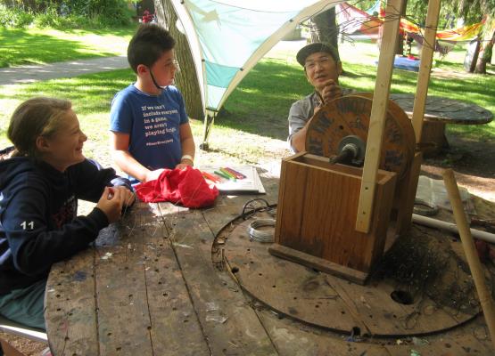 Two campers at table work with wire and talk to artist