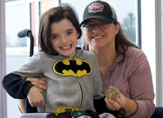 Girl wearing batman shirt in wheelchair with mom holding a clay art piece