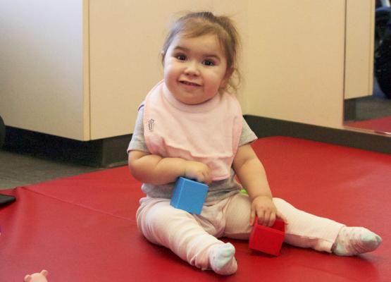 Toddler girl on red mat with toys