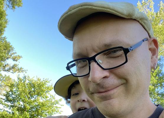 Man with glasses and cap and small boy learning over his shoulder