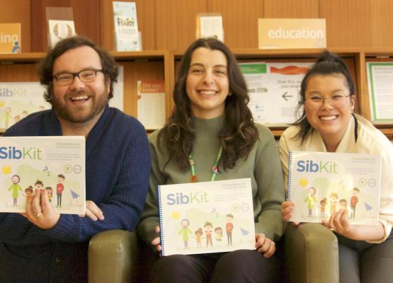 Three young adults hold colourful booklet and smile