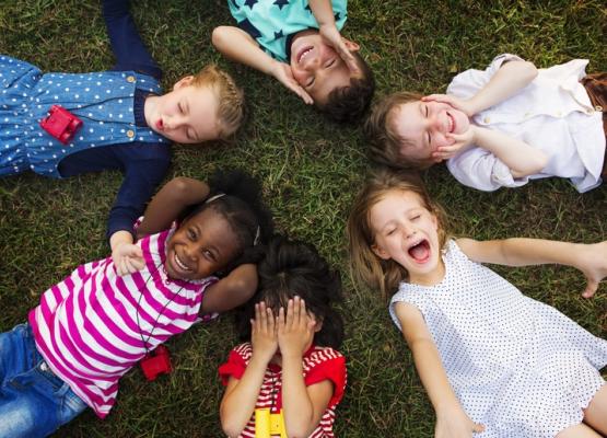 Six young kids lying on the grass smiling and expressive face