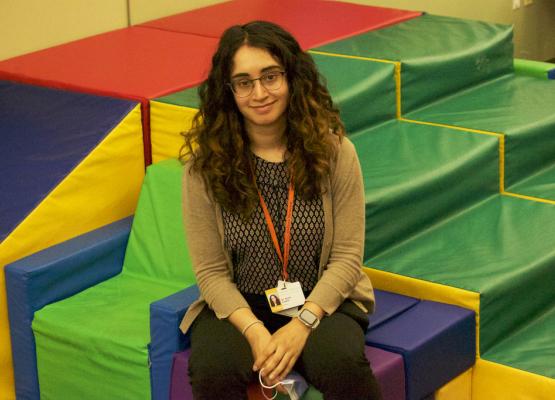 Woman with long dark wavey hair smiles sitting on colourful play structure