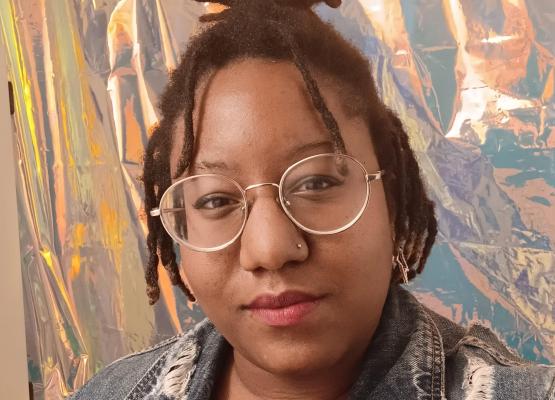 Young woman with glasses and twists in hair against backdrop of abstract painting
