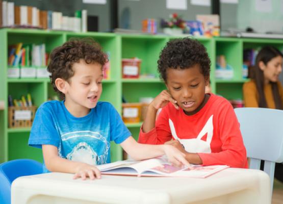 Two boys in bright shirts look at book in classsroom