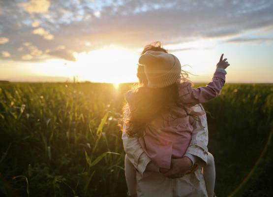 Woman holding girl in field with sun shining
