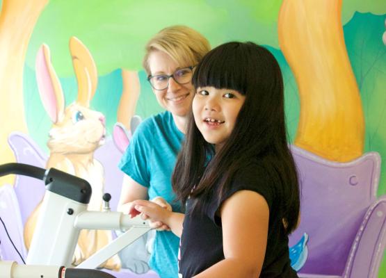 Girl with long black hair with bangs smiles on treadmill with woman with blonde hair holding her hand