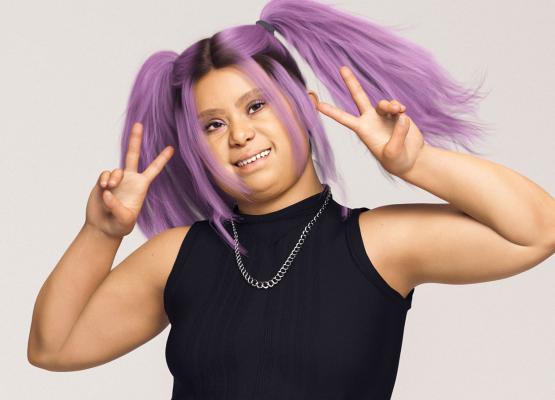 Woman with purple hair and black shirt smiles and holds up two peace signs