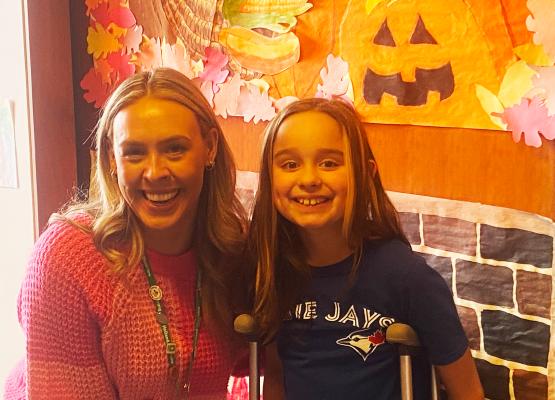 Young woman with long blonde hair beside girl with long blonde hair smiling in front of Halloween decorations