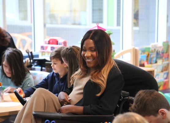 Woman in a wheelchair surrounded by students in a classroom