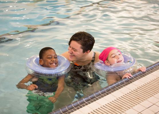 Two young kids at pool's edge with an adult