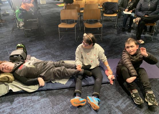 Young man lies on floor beside a woman and man with chairs lined behind them