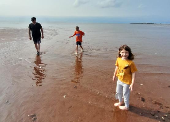 Girl in yellow shirt in water with red soil with man and boy behind her